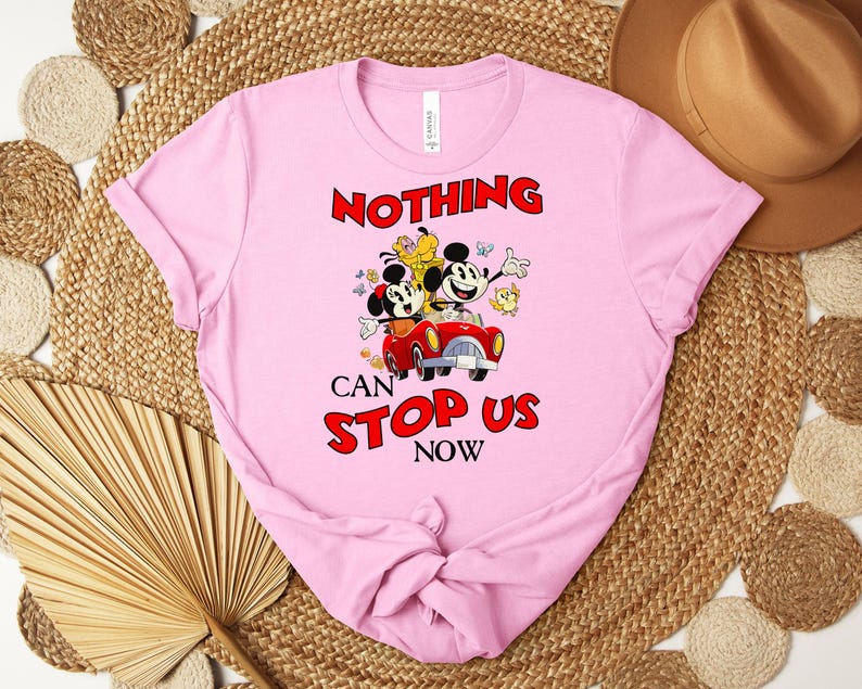 Puede incluir: Camiseta rosa claro con un dibujo animado de Mickey y Minnie Mouse en un coche rojo, con el texto "NOTHING CAN STOP US NOW" en rojo. La camiseta est&aacute; hecha de material suave.