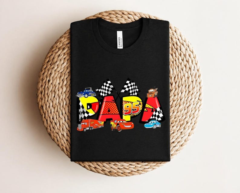 Puede incluir: Camiseta negra con la palabra "DAPA" en un dise&ntilde;o colorido con coches de carreras y el n&uacute;mero 95. El dise&ntilde;o incluye banderas a cuadros y varias ilustraciones de coches, creando un aspecto l&uacute;dico y vibrante.