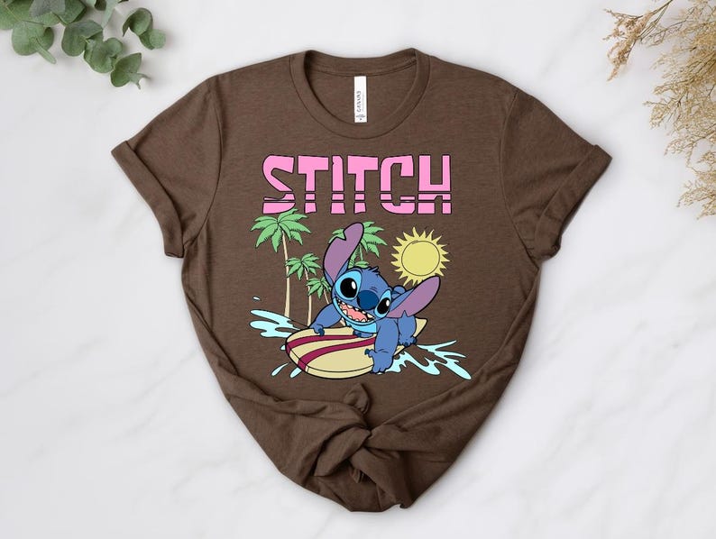 May include: Brown t-shirt featuring a graphic of Stitch surfing on a surfboard. The word "STITCH" is printed in pink above the character. Palm trees and a yellow sun are also included in the design.