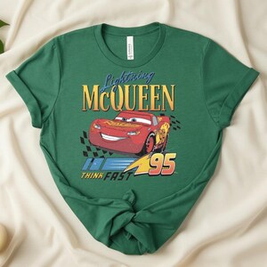 May include: Green t-shirt featuring Lightning McQueen from the movie Cars. The design includes the character's image, the text "Lightning McQueen", and the number "95". The phrase "Think Fast" is also included in the design.