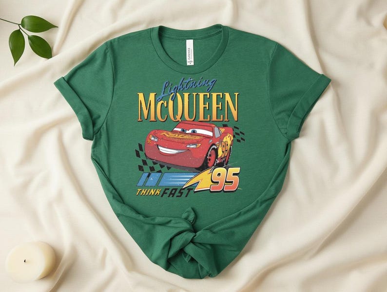 May include: Green t-shirt featuring Lightning McQueen from the movie Cars. The design includes the character's image, the text "Lightning McQueen", and the number "95". The phrase "Think Fast" is also included in the design.