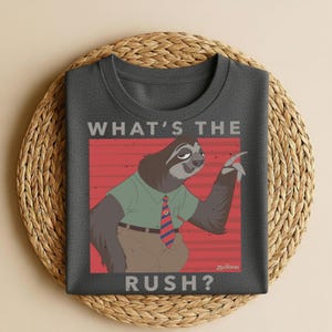 May include: Dark gray t-shirt featuring a cartoon sloth character with the text "WHAT'S THE RUSH?" The sloth is wearing a green shirt, a red and blue striped tie, and brown pants. The design is set against a red background with horizontal lines.