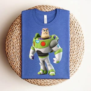 May include: A blue t-shirt featuring a graphic of Buzz Lightyear from Toy Story. The character is depicted in his signature green, white, and purple spacesuit. The shirt is made of a soft material and is suitable for casual wear.