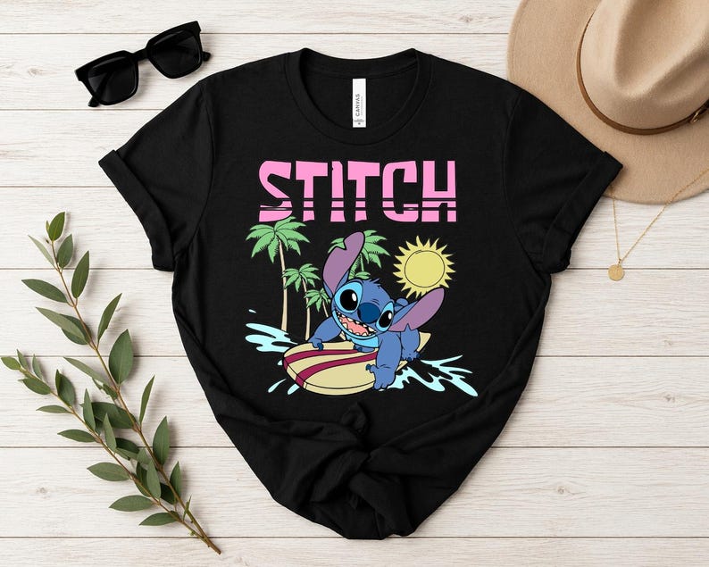 May include: Black t-shirt featuring a graphic of Stitch surfing on a surfboard, with palm trees and a sun in the background. The word "STITCH" is printed in pink block letters above the graphic.