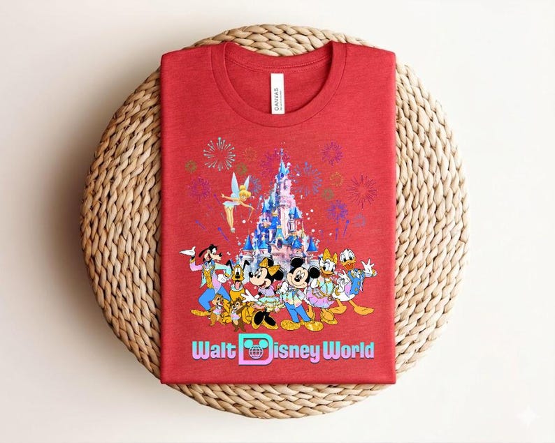 Może przedstawiać: Czerwona koszulka z kolorową grafiką postaci Disneya, w tym Myszki Miki i Minnie, Kaczora Donalda i Goofiego, na tle zamku i fajerwerk&oacute;w. Tekst "Walt Disney World" jest wyświetlany poniżej.