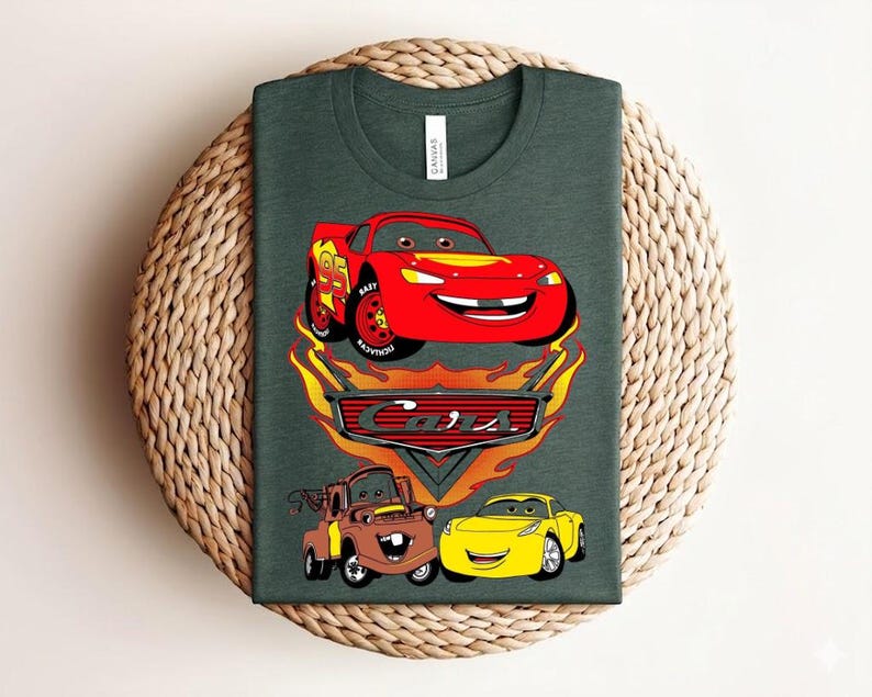 May include: Dark green t-shirt featuring a graphic of characters from the animated movie "Cars." The design includes a red race car, a brown truck, and a yellow car, with the word "Cars" in a stylized font.