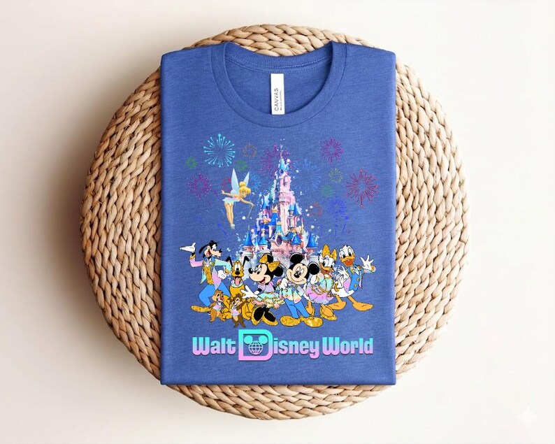 Może przedstawiać: Niebieska koszulka z kolorową grafiką postaci Disneya, zamkiem, fajerwerkami i napisem "Walt Disney World". Projekt zawiera Myszkę Miki i Minnie, Kaczora Donalda i Goofy'ego.