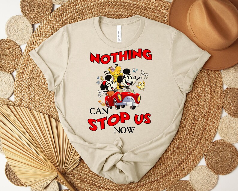 Puede incluir: Camiseta beige con una ilustraci&oacute;n de dibujos animados de Mickey y Minnie Mouse en un coche rojo, con el texto rojo "NOTHING CAN STOP US NOW". La camiseta tiene cuello redondo y mangas cortas.