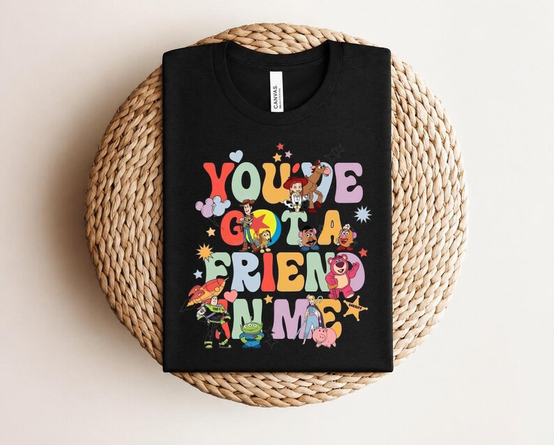 May include: Black t-shirt with the phrase "You've Got a Friend in Me" in colourful, retro lettering. The design features cartoon characters from a popular animated film. A fun, playful design for fans of the film.