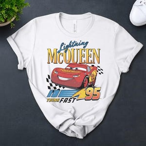 May include: White t-shirt with a distressed graphic of Lightning McQueen from the Cars film. The design includes the text "Lightning McQueen", the number "95", and the phrase "Think Fast".