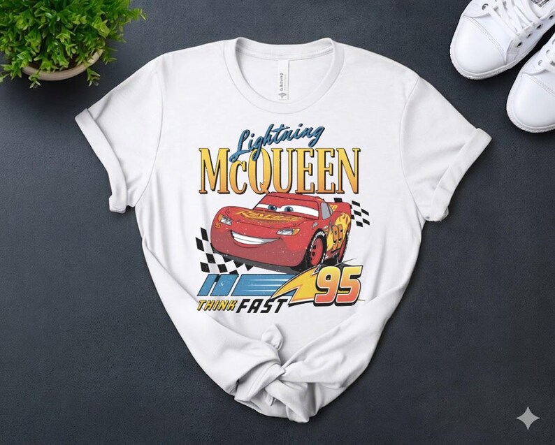May include: White t-shirt with a distressed graphic of Lightning McQueen from the Cars film. The design includes the text "Lightning McQueen", the number "95", and the phrase "Think Fast".