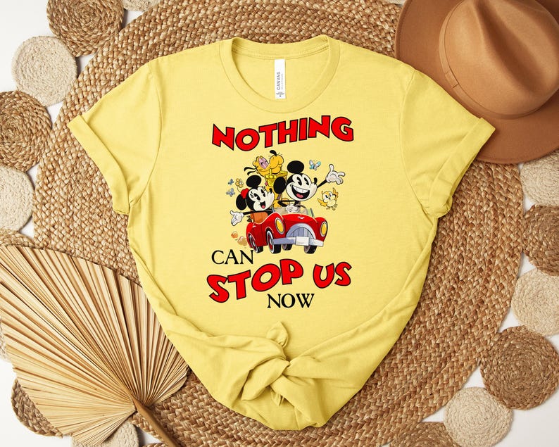 Puede incluir: Camiseta amarilla con un gr&aacute;fico de dibujos animados de Mickey y Minnie Mouse en un coche rojo, con el texto "NOTHING CAN STOP US NOW" en rojo. El dise&ntilde;o incluye otros personajes de dibujos animados y mariposas.