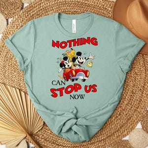 Puede incluir: Camiseta verde claro con Mickey y Minnie Mouse en un coche rojo, con el texto "NOTHING CAN STOP US NOW" en rojo. La camiseta tiene cuello redondo y mangas cortas.