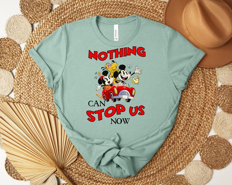 Puede incluir: Camiseta verde claro con Mickey y Minnie Mouse en un coche rojo, con el texto "NOTHING CAN STOP US NOW" en rojo. La camiseta tiene cuello redondo y mangas cortas.