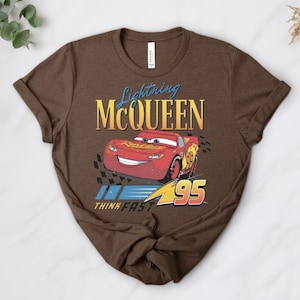 May include: A brown t-shirt with a graphic of Lightning McQueen, a red race car, and the text "Lightning McQueen" above the car and "Think Fast" below. The number "95" is displayed.