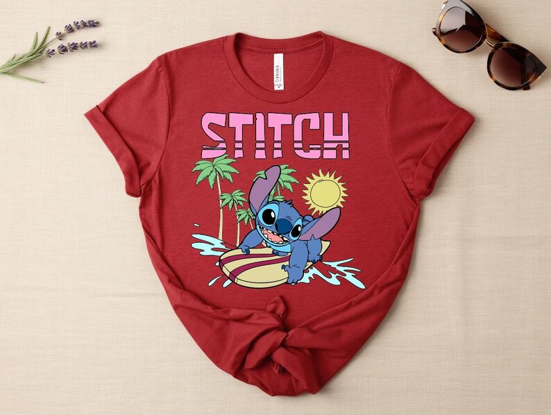 May include: Red t-shirt featuring the word "STITCH" in pink block letters. The shirt has a graphic of the character Stitch surfing on a surfboard, with palm trees and a sun in the background. Sunglasses are on the top right.