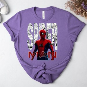 Peut inclure: Un t-shirt &agrave; manches courtes lavande avec un graphique du personnage Spider-Man en costume rouge et bleu. Le mot SPIDER est imprim&eacute; en blanc sur un fond de bande dessin&eacute;e en noir et blanc, et le mot MAN est imprim&eacute; en rouge en dessous.