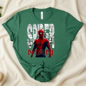 Peut inclure: Un t-shirt &agrave; manches courtes vert for&ecirc;t avec un graphisme du personnage Spider-Man en costume rouge et bleu. Le mot SPIDER est imprim&eacute; en blanc sur un fond de bande dessin&eacute;e, et le mot MAN est imprim&eacute; en lettres rouges grasses en dessous.