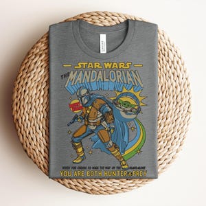 K&ouml;nnte beinhalten: Graues T-Shirt mit einer Grafik von The Mandalorian aus Star Wars. Das Design enth&auml;lt den Text "STAR WARS - THE MANDALORIAN" und das Zitat "WHEN YOU CHOOSE TO WALK THE WAY OF THE MANDALORE YOU ARE BOTH HUNTER & PREY."