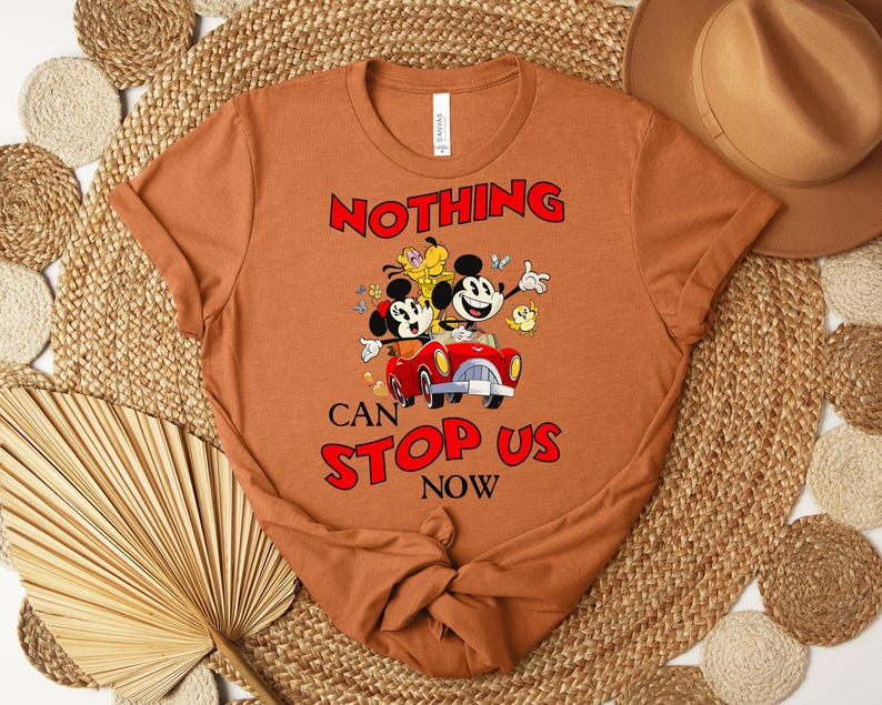 Puede incluir: Camiseta de color &oacute;xido con un gr&aacute;fico de Mickey y Minnie Mouse en un coche rojo, con el texto "NOTHING CAN STOP US NOW" en rojo. El dise&ntilde;o incluye flores y mariposas de dibujos animados. La camiseta se muestra sobre una estera tejida.