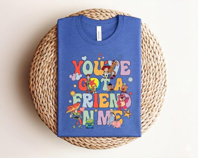 May include: Blue t-shirt with the phrase "You've Got a Friend in Me" in colourful, retro lettering. The shirt features cartoon characters. The t-shirt is made of a soft material.