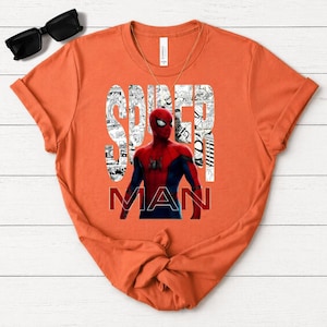 Peut inclure: Un t-shirt orange &agrave; manches courtes avec un motif de Spider-Man en costume rouge et bleu. Le mot SPIDER est imprim&eacute; en grandes lettres blanches remplies de panneaux de bande dessin&eacute;e en noir et blanc, et le mot MAN est imprim&eacute; en rouge.