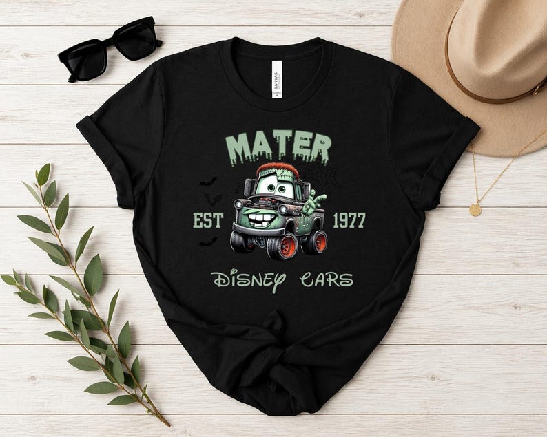 Może przedstawiać: Czarny t-shirt z grafiką Matera z filmu Auta Disneya w stylu zombie. Projekt zawiera napisy "MATER", "EST 1977" i "Disney Cars". Koszulka ma okrągły dekolt i kr&oacute;tkie rękawy.