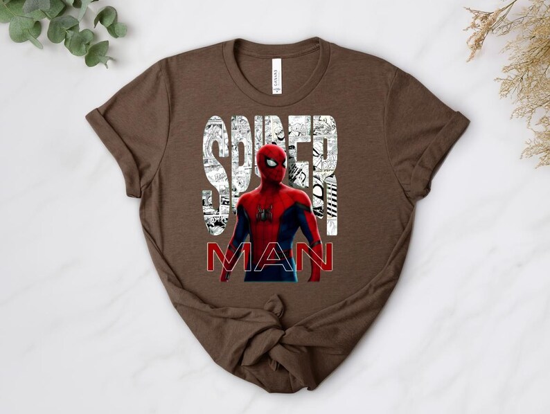 Peut inclure: Un t-shirt marron &agrave; manches courtes avec une illustration du personnage Spider-Man en costume rouge et bleu. Le mot SPIDER est imprim&eacute; en grandes lettres blanches remplies de cases de bande dessin&eacute;e, et MAN est en rouge.