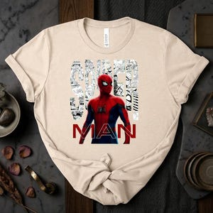 Peut inclure: Un t-shirt beige &agrave; manches courtes avec un graphisme de Spider-Man en costume rouge et bleu. Le mot SPIDER est &eacute;crit dans une police blanche style bande dessin&eacute;e, et le mot MAN est imprim&eacute; en lettres rouges grasses sous le personnage.