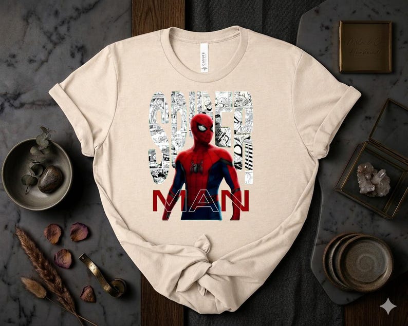 Peut inclure: Un t-shirt beige &agrave; manches courtes avec un graphisme de Spider-Man en costume rouge et bleu. Le mot SPIDER est &eacute;crit dans une police blanche style bande dessin&eacute;e, et le mot MAN est imprim&eacute; en lettres rouges grasses sous le personnage.