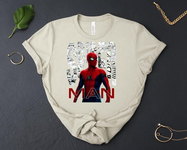 Peut inclure: Un t-shirt beige &agrave; manches courtes avec un graphisme du personnage Spider-Man en costume rouge et bleu. Le mot SPIDER est rempli de panneaux de bande dessin&eacute;e en noir et blanc, et le mot MAN est imprim&eacute; en lettres rouges sous la figure.