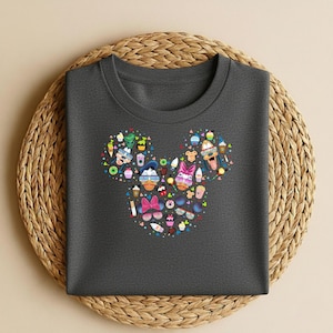 May include: Dark grey t-shirt with a Mickey Mouse head design made up of cartoon characters, sunglasses, ice cream, and other colourful summer-themed graphics. The shirt is on a woven, circular placemat.