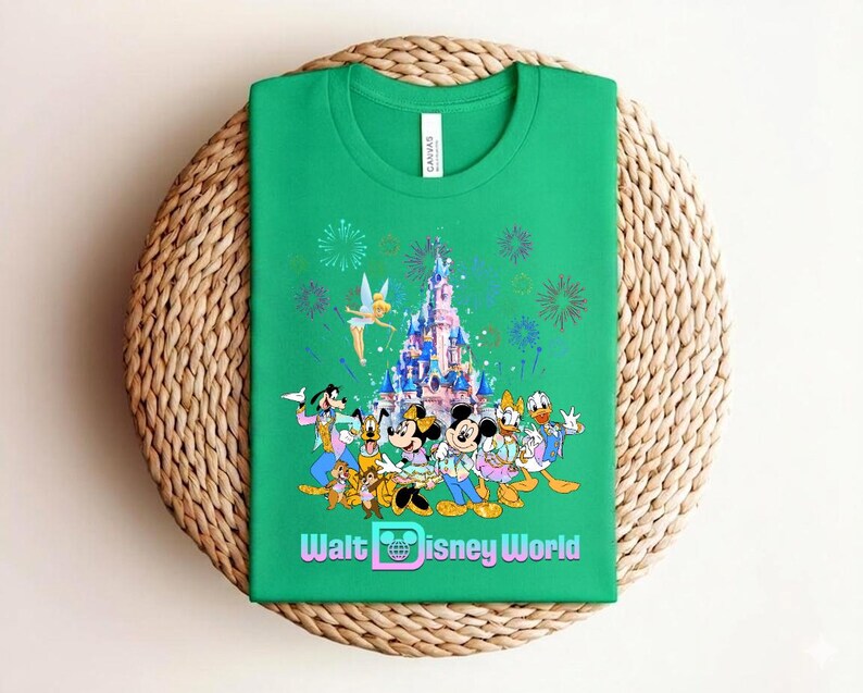 Może przedstawiać: Zielona koszulka z kolorową grafiką postaci Disneya, zamkiem, fajerwerkami i napisem "Walt Disney World". Projekt zawiera Myszkę Miki i Minnie, Kaczora Donalda i Goofy'ego.
