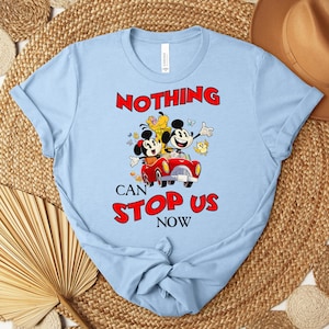 Puede incluir: Camiseta azul claro con un gr&aacute;fico de Mickey y Minnie Mouse en un coche rojo, con el texto "NOTHING CAN STOP US NOW" en rojo. El dise&ntilde;o incluye otros personajes de dibujos animados y es un dise&ntilde;o l&uacute;dico y colorido.