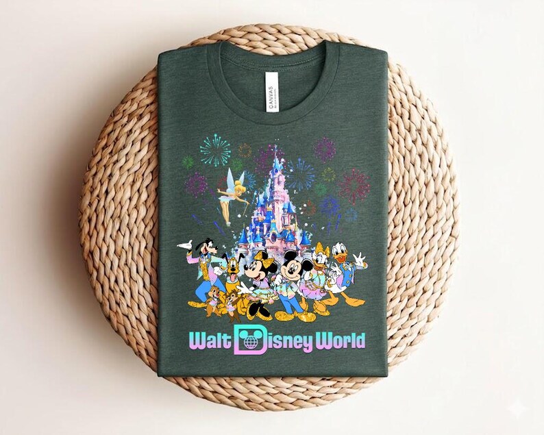 Może przedstawiać: Ciemnozielona koszulka z kolorową grafiką postaci Disneya, w tym Myszki Miki i Minnie, Kaczora Donalda i Goofy'ego, na tle zamku i fajerwerk&oacute;w. Tekst "Walt Disney World" jest wyświetlany poniżej.