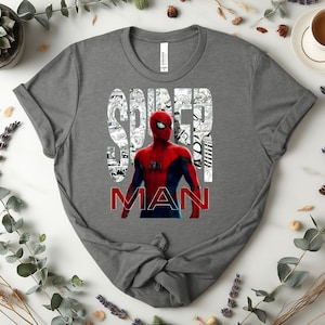 Peut inclure: Un t-shirt gris fonc&eacute; &agrave; manches courtes avec un motif du personnage Spider-Man en rouge et bleu. Le mot SPIDER est imprim&eacute; en blanc sur un fond de cases de bande dessin&eacute;e, et le mot MAN est imprim&eacute; en lettres rouges grasses en dessous.