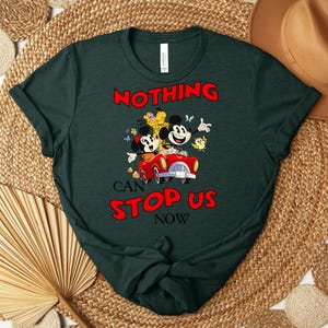 Puede incluir: Camiseta verde oscuro con un dise&ntilde;o de dibujos animados de Mickey y Minnie Mouse en un coche rojo, con el texto "NOTHING CAN STOP US NOW" en rojo. La camiseta tiene cuello redondo y mangas cortas.