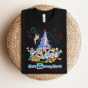 Może przedstawiać: Czarny t-shirt z kolorową grafiką postaci Disneya, zamkiem i fajerwerkami, z napisem "Walt Disney World". Projekt zawiera Myszkę Miki, Minnie, Kaczora Donalda i inne popularne postacie.