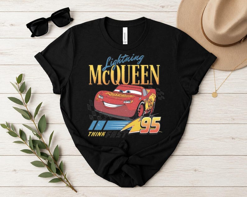 May include: Black t-shirt with a graphic of Lightning McQueen from the Cars film. The design includes the text "Lightning McQueen" in yellow and blue, the number "95", and the phrase "Think Fast".