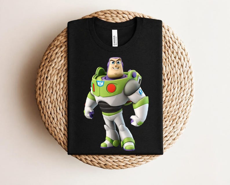 May include: Black t-shirt featuring a colorful graphic of Buzz Lightyear from Toy Story. The character is depicted in his signature green, white, and purple spacesuit. The shirt is displayed on a woven, circular surface.