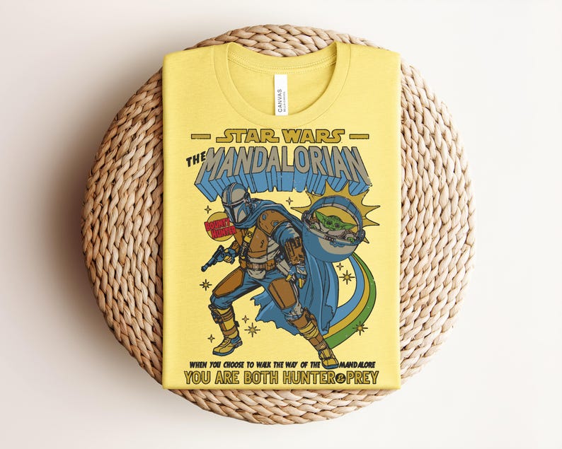 K&ouml;nnte beinhalten: Gelbes T-Shirt mit einer Grafik von The Mandalorian aus Star Wars. Das Design enth&auml;lt den Text "STAR WARS THE MANDALORIAN" und das Zitat "WHEN YOU CHOOSE TO WALK THE WAY OF THE MANDALORE YOU ARE BOTH HUNTER PREY". Die Illustration zeigt den Mandalorianer mit Grogu.