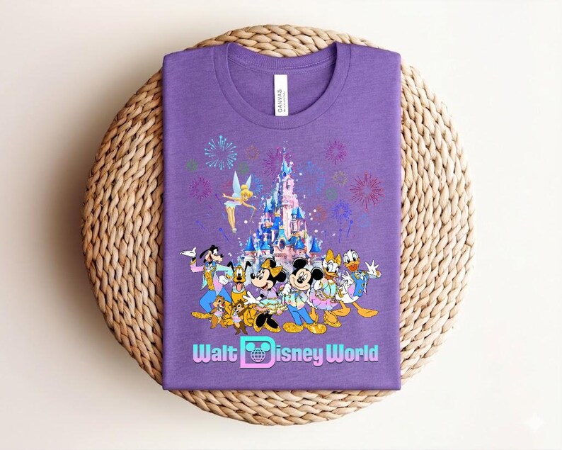 Może przedstawiać: Fioletowa koszulka z kolorową grafiką postaci Disneya, w tym Myszki Miki, Myszki Minnie, Kaczora Donalda i Goofy'ego, na tle zamku i fajerwerk&oacute;w. Tekst "Walt Disney World" jest wyświetlany na dole.