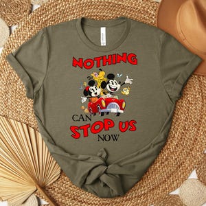 Puede incluir: Camiseta verde oliva con un dise&ntilde;o de Mickey y Minnie Mouse en un coche rojo, con el texto "NOTHING CAN STOP US NOW". El dise&ntilde;o incluye otros personajes de dibujos animados y flores. La camiseta es de material suave.