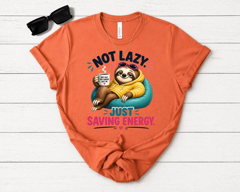 May include: Orange t-shirt featuring a sloth in sunglasses and a yellow hoodie, holding a coffee mug. The text says "NOT LAZY JUST SAVING ENERGY."