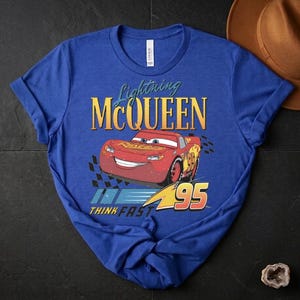 May include: Blue t-shirt with a graphic of Lightning McQueen from the Cars film. The design includes the text "Lightning McQueen", a red race car graphic, and the number "95". The phrase "THINK FAST" is also included.