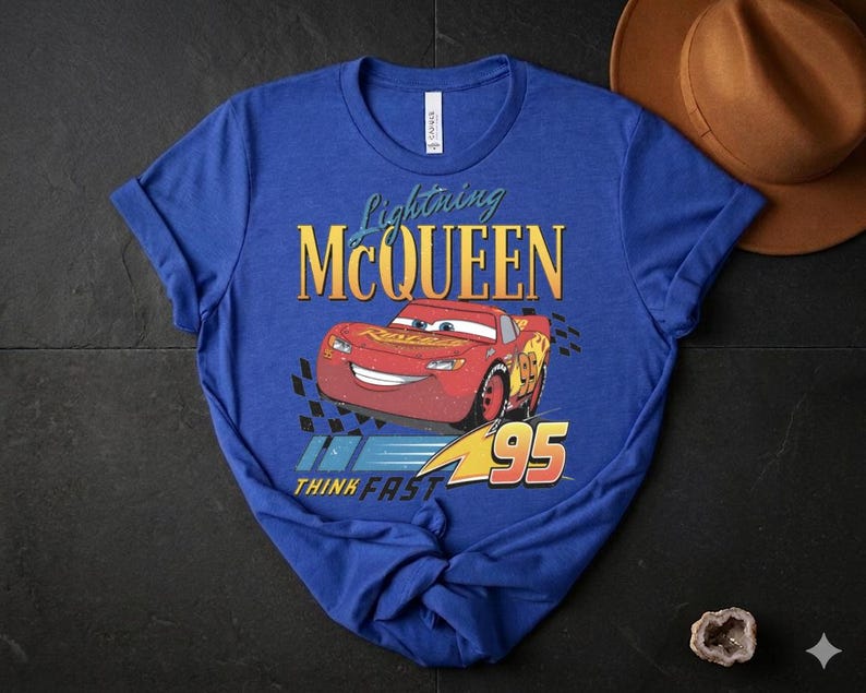 May include: Blue t-shirt with a graphic of Lightning McQueen from the Cars film. The design includes the text "Lightning McQueen", a red race car graphic, and the number "95". The phrase "THINK FAST" is also included.