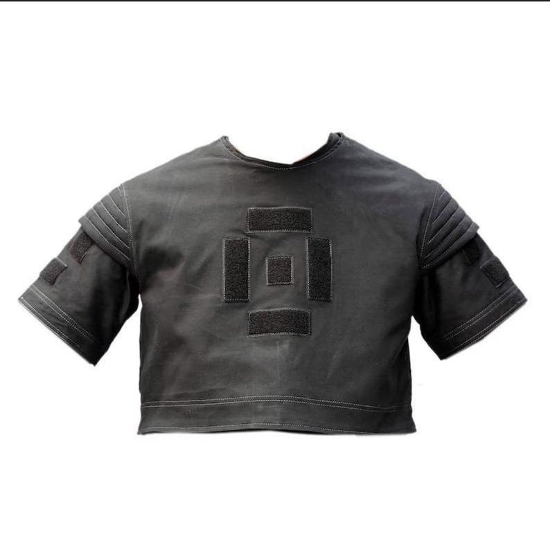 Puede incluir: Una parte superior corta de color gris oscuro con mangas cortas. La parte superior presenta un dise&ntilde;o geom&eacute;trico en la parte delantera hecho de parches negros. Las mangas tienen un dise&ntilde;o en capas con parches negros adicionales. Las costuras blancas delinean los bordes.