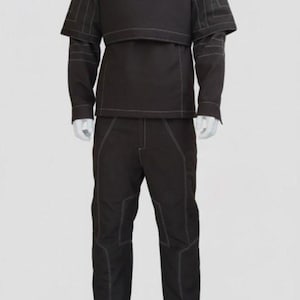 Puede incluir: Un conjunto negro que consta de una chaqueta de cuello alto con hombreras, un chaleco a juego, una camisa de manga larga y pantalones. El conjunto presenta costuras blancas y se muestra en un maniqu&iacute;.