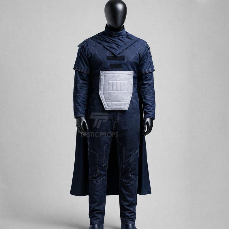 Puede incluir: Un disfraz azul oscuro exhibido en un maniqu&iacute;. El atuendo incluye una parte superior de manga larga con cuello alto, una pieza de pecho gris claro y pantalones a juego. Una capa azul oscuro est&aacute; drapeada sobre los hombros. El disfraz es probablemente para cosplay o una producci&oacute;n teatral.