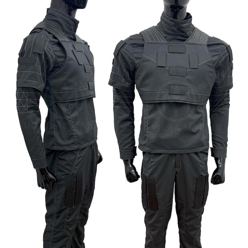 May include: Black tactical outfit, featuring a high-collared jacket with a layered chest piece and matching pants. The jacket has long sleeves and reinforced shoulder details. The pants have multiple pockets. The outfit is displayed on a mannequin.